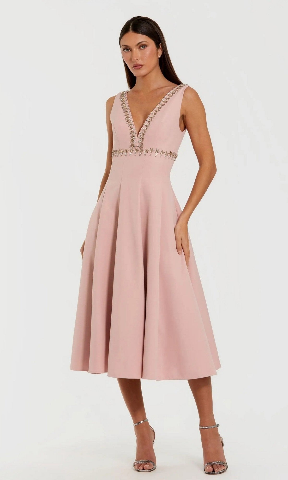 Woman in a sleeveless, V-neck dusty rose Mac Duggal 21159 midi dress featuring beaded accents at the neckline and waist, posing with one hand in her pocket—an elegant pick for a wedding guest.